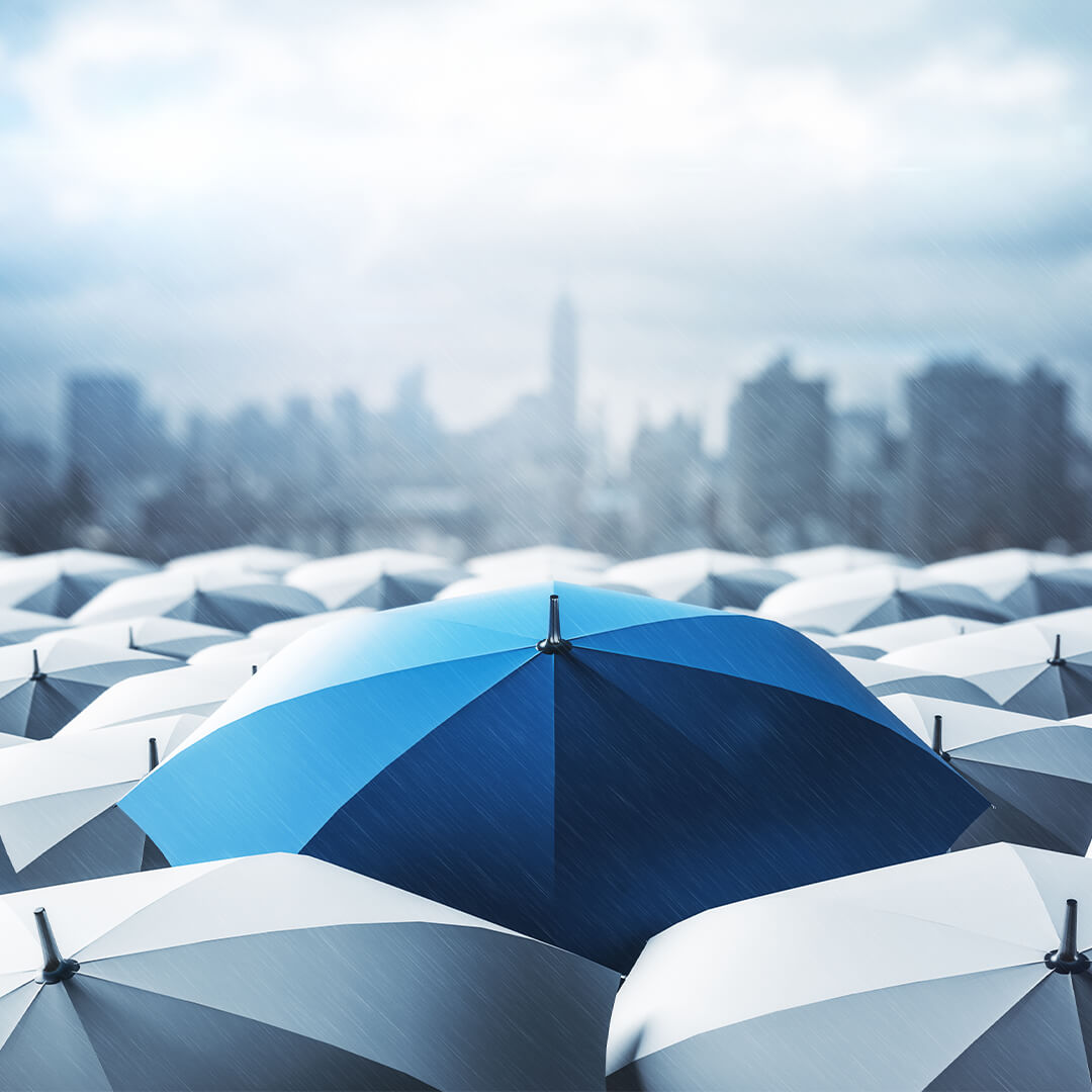 Parapluie bleu se détachant sur de nombreux parapluies gris sous la pluie avec la ville en arrière-plan - Odgers Executive Search Board Headhunters