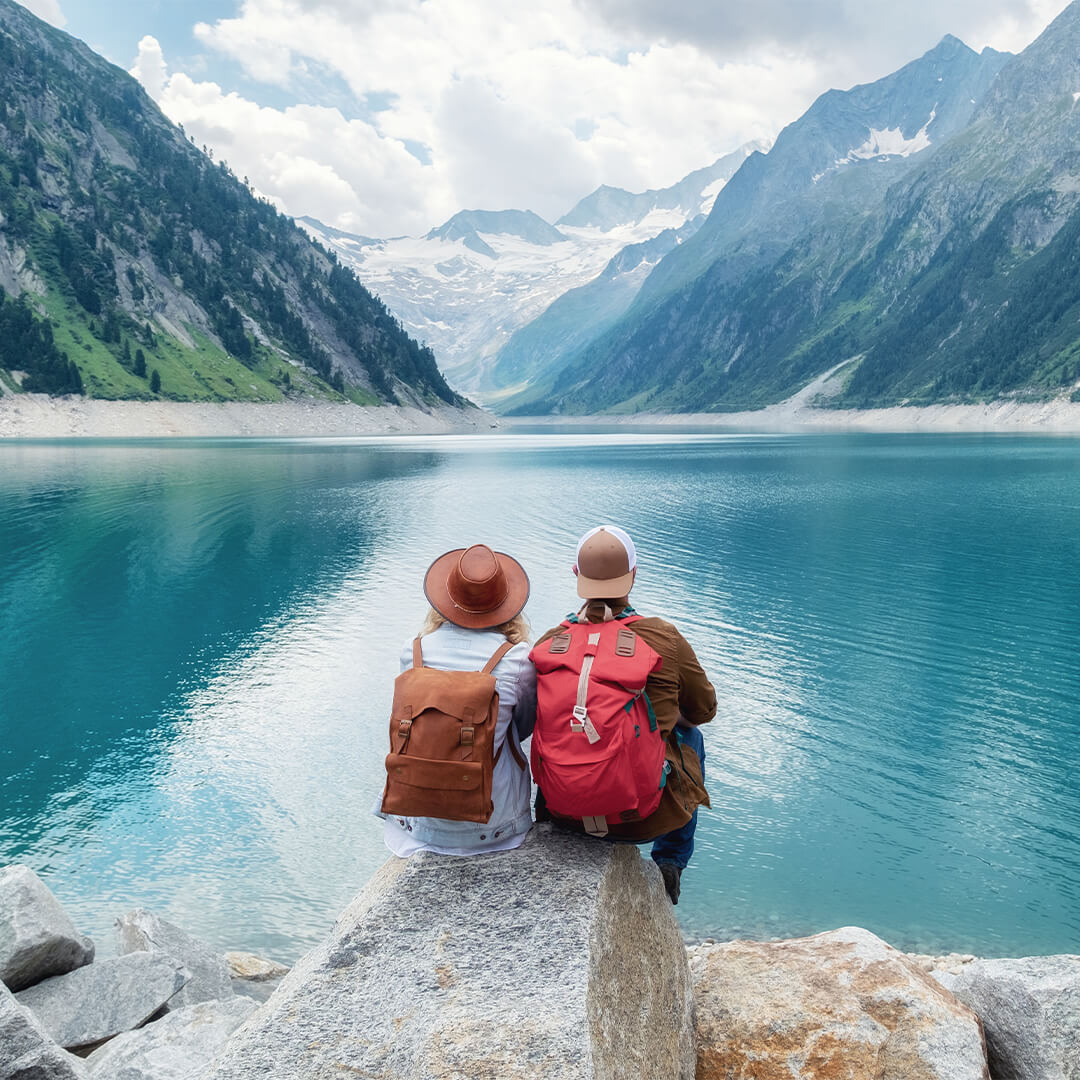 Pareja con sombreros y mochilas mirando hacia un lago azul brillante con montañas al fondo - Odgers Executive Search Board Headhunters