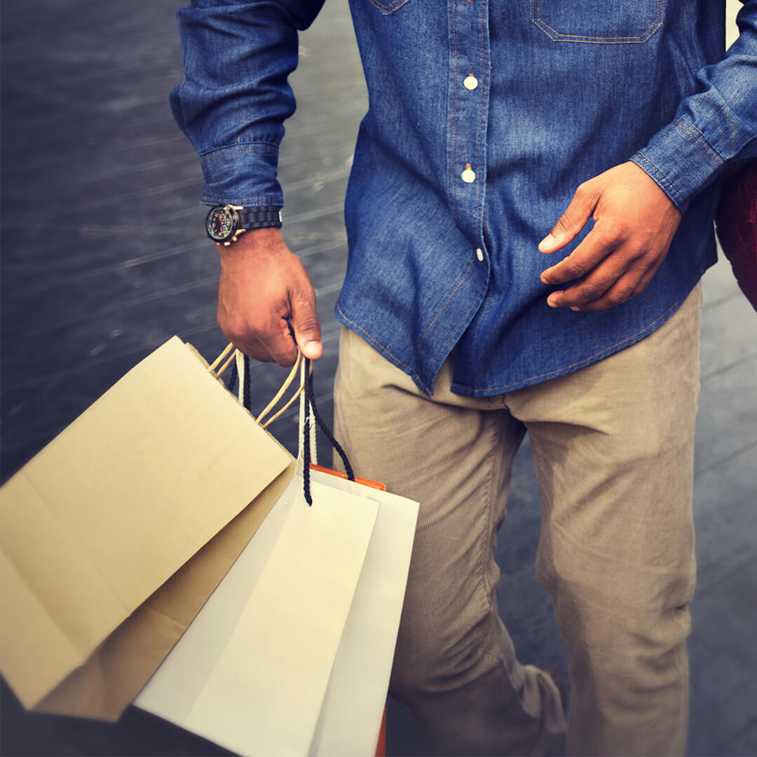 Man in crèmekleurige broek en blauw overhemd met zwart horloge draagt ​​boodschappentassen - Odgers Executive Search Board Headhunters